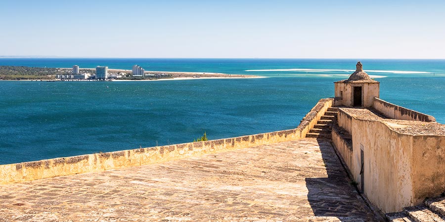 The stone terrace and guardhouse of the Fort of São Filipe in Setúbal overlooks the blue sea on a sunny day. 